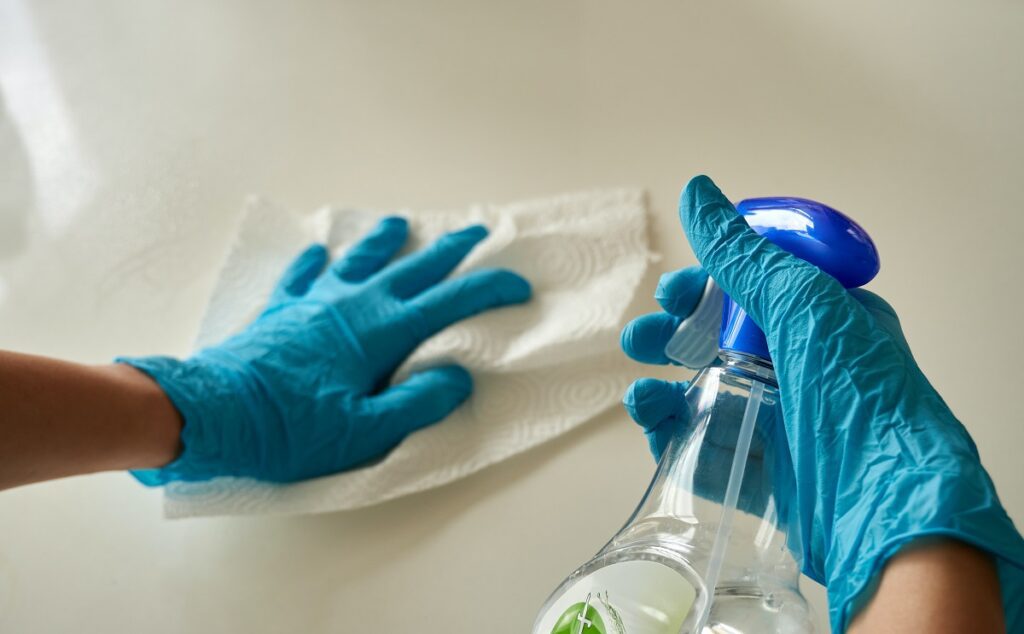 A person wearing gloves and cleaning a table with a spray and tissue paper  