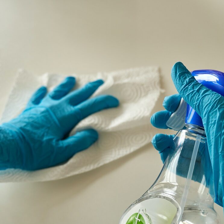 A person wearing gloves and cleaning a table with a spray and tissue paper  