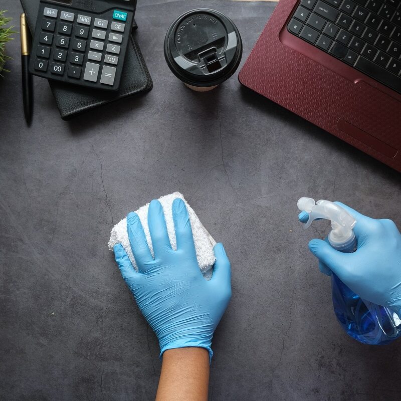 A person cleaning a table with a laptop, coffee, calculator, and pen on top.